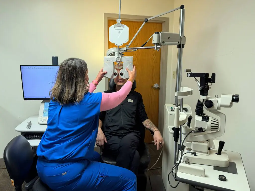 Optometric technician adjusting a phoropter for a patient during a comprehensive eye exam at Maple Grove Eye Doctors