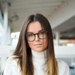 Woman with straight dark hair wearing white turtleneck sweater posing wearing round plastic frame Maple Grove Eye Doctors at Pearle Vision