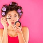 Women putting on mascara with compact mirror and curlers in her brown hair Maple Grove Eye Doctors at Pearle Vision