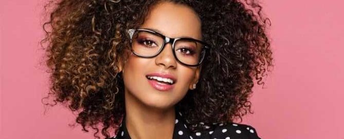 Designer black plastic Eyeglass Frame on Female with very curly big hair . Maple Grove Eye Doctors at Pearle Vision