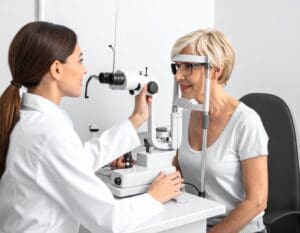 Woman at equipment with Doctor having a comprehensive eye exam. Maple Grove Eye Doctors at Pearle Vision